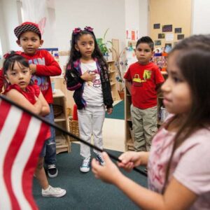 a young group of children stand in a Pre-K 4 SA classroom, one child holds an American flag