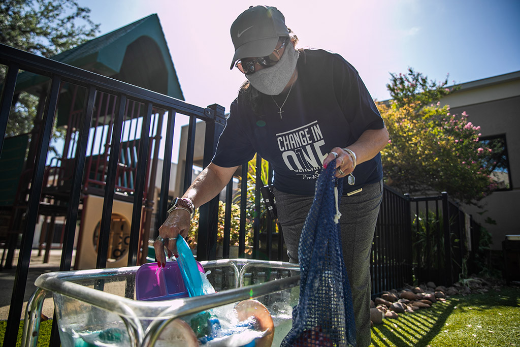 An Adult pulls soapy dishes from a bin outside near a playground