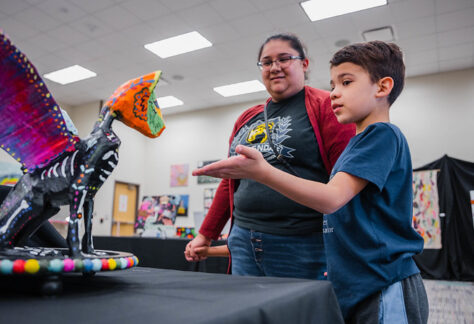 student reaches a hand out to an artwork of a dragon