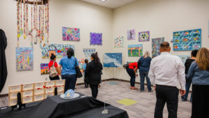 adults gather around a museum style exhibition of student artwork