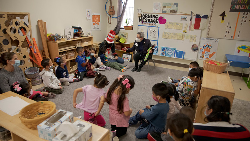 An educator sits on the floor of a Pre-K 4 SA classroom and reads a book to young students.