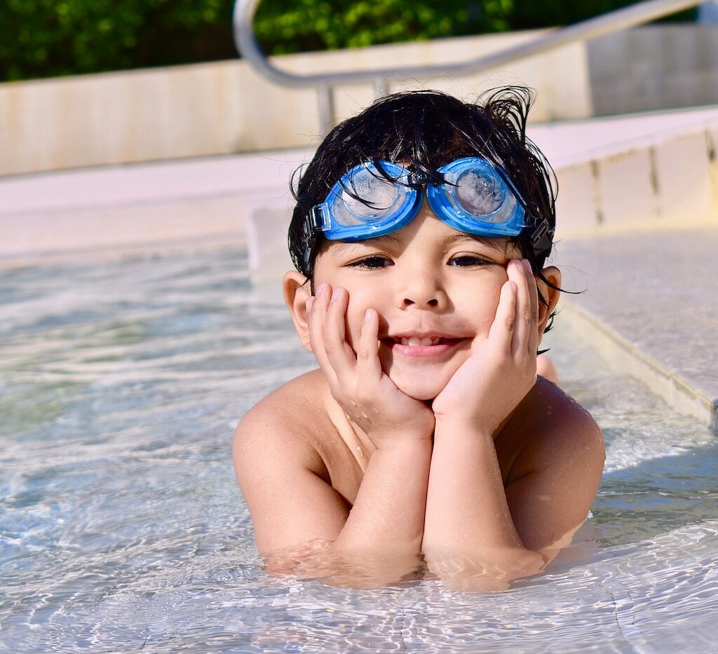 a young child smiles at the camera while lounging in a shallow pool