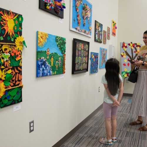 a child and an adult look at artworks on the wall