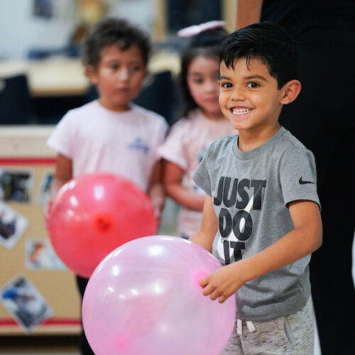 a young boy smiles while playing with a large pink balloon