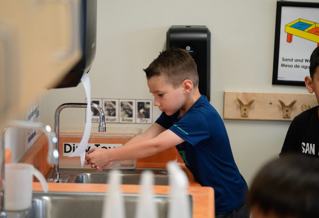 a young boy washes his hands in a classroom