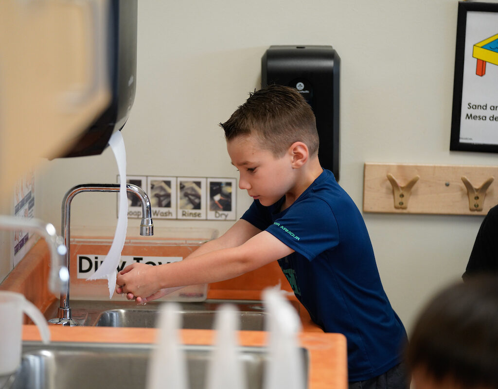 a young boy washes his hands in a classroom