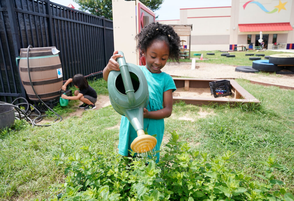 a young girl waters plants in a garden oustide a Pre-K 4 SA center