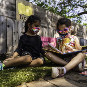two young girls read a book outside
