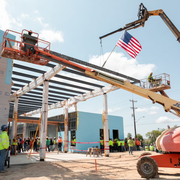 A crane raises a steel beam at a construction site with an American flag.