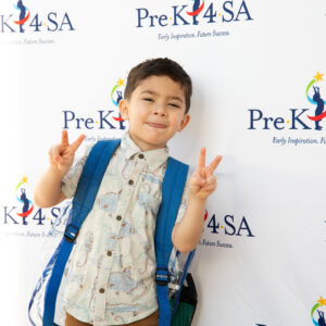 A young boy throws up two peace signs on his first day of school at Pre-K 4 SA.