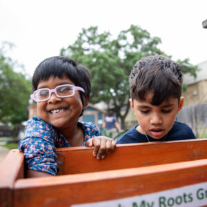 Two young children reach into a container in a garden