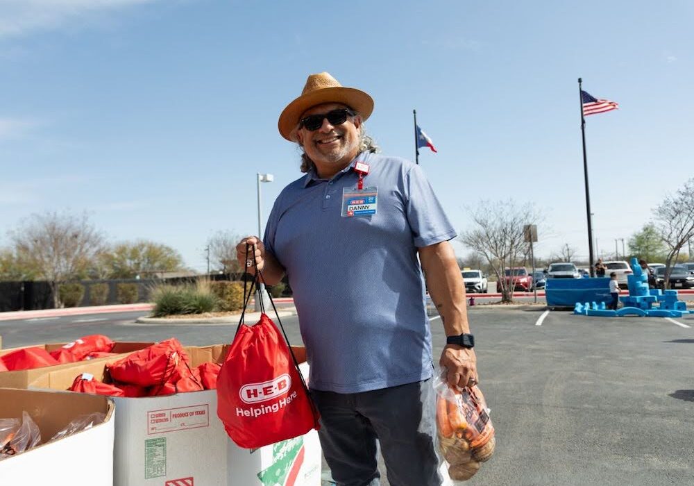 A man in a hat and sunglasses standing next to a pile of food
