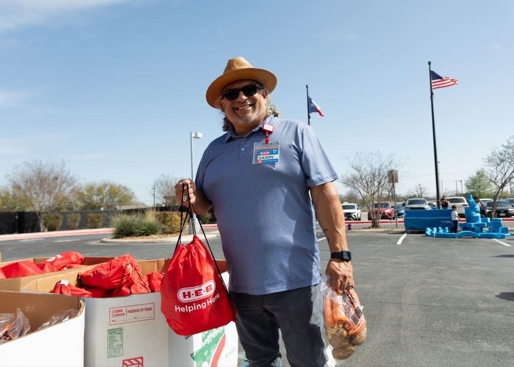 H-E-B Produce giveaway A man in a hat and sunglasses standing next to a pile of food