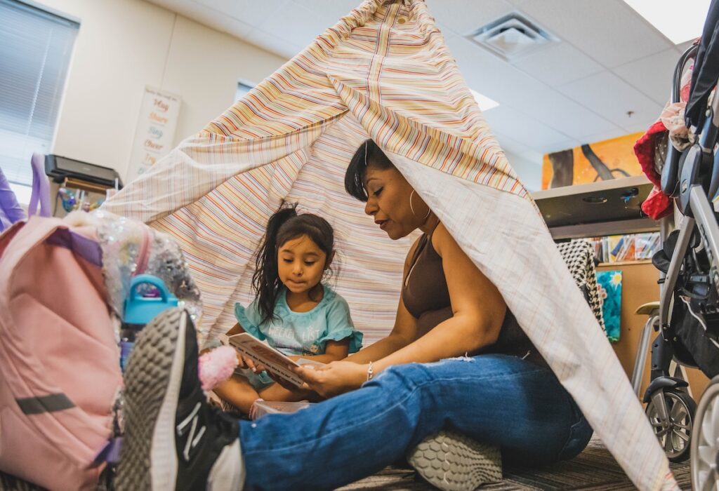 Adult and child reading inside a makeshift tent in a classroom setting.