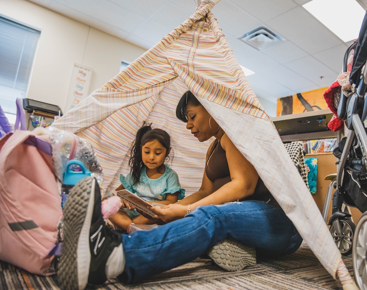 Adult and child reading inside a makeshift tent in a classroom setting.