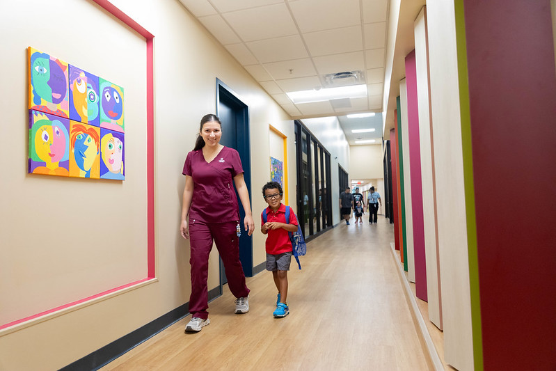 Teacher walking with a young student in a colorful school hallway.