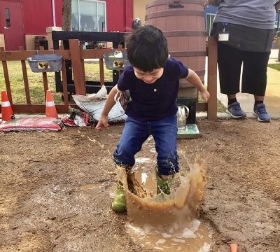 a young child stomps in a muddy puddle