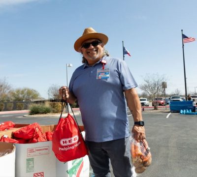 A man in a hat and sunglasses standing next to a pile of food