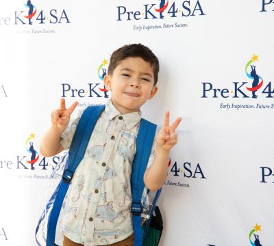 A young boy throws up two peace signs on his first day of school at Pre-K 4 SA.