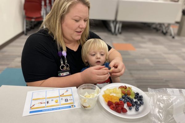 An adult helps a child eat a plate of fruit