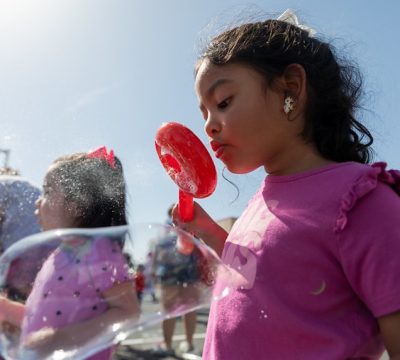 a young girl blows large bubbles against a sunny sky