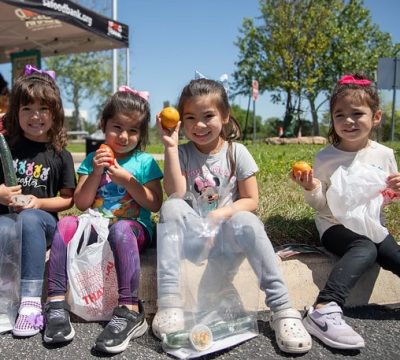 four children sit on the curb and hold up oranges