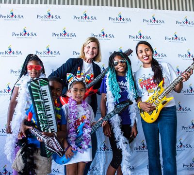 children and adults pose in front of a step and repeat with colorful blow up guitars and props