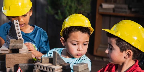 Three children wearing hard hats and playing with wooden blocks